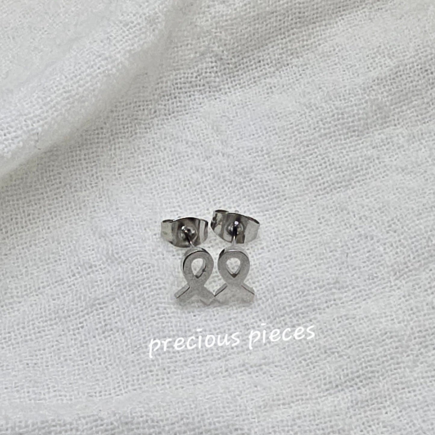 Silver earrings on a white fabric background with 'precious pieces' text.