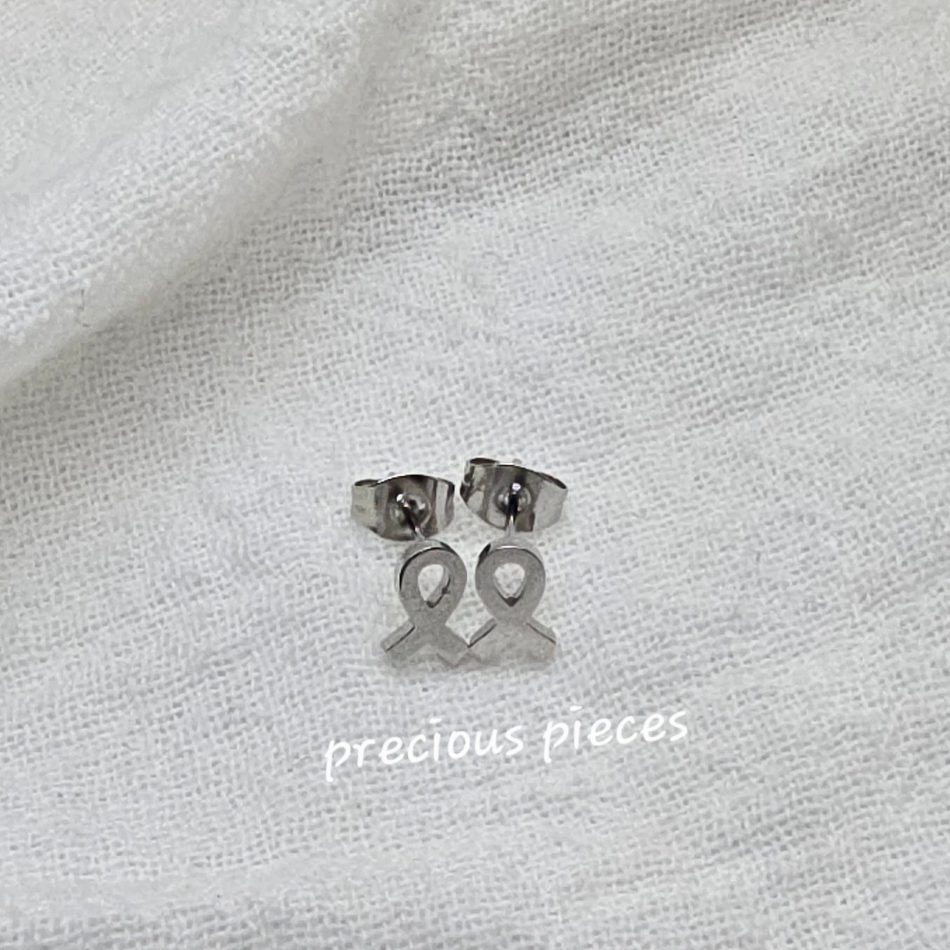 Silver earrings on a white fabric background with 'precious pieces' text.