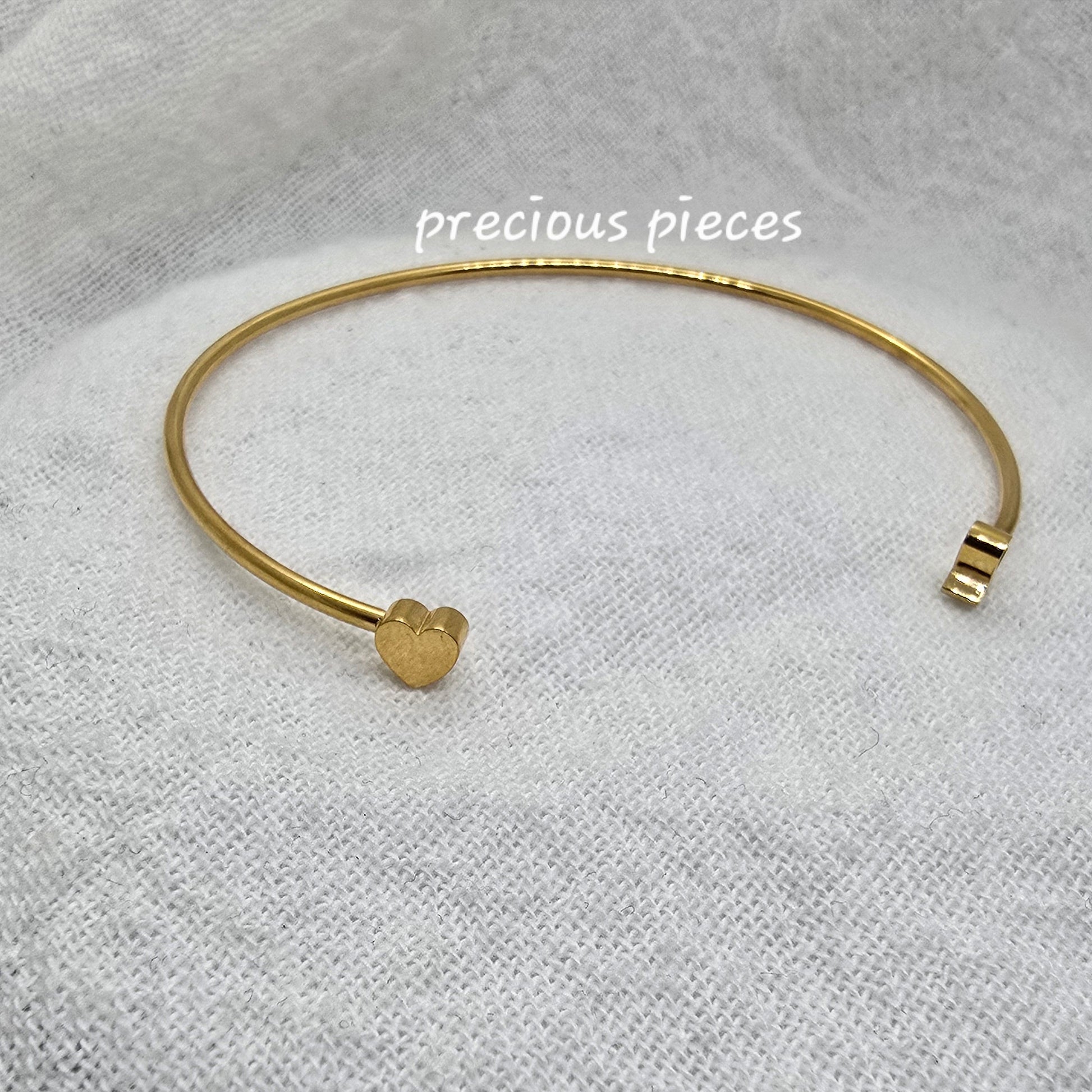 Gold bracelet on a textured white fabric background with 'precious pieces' text.
